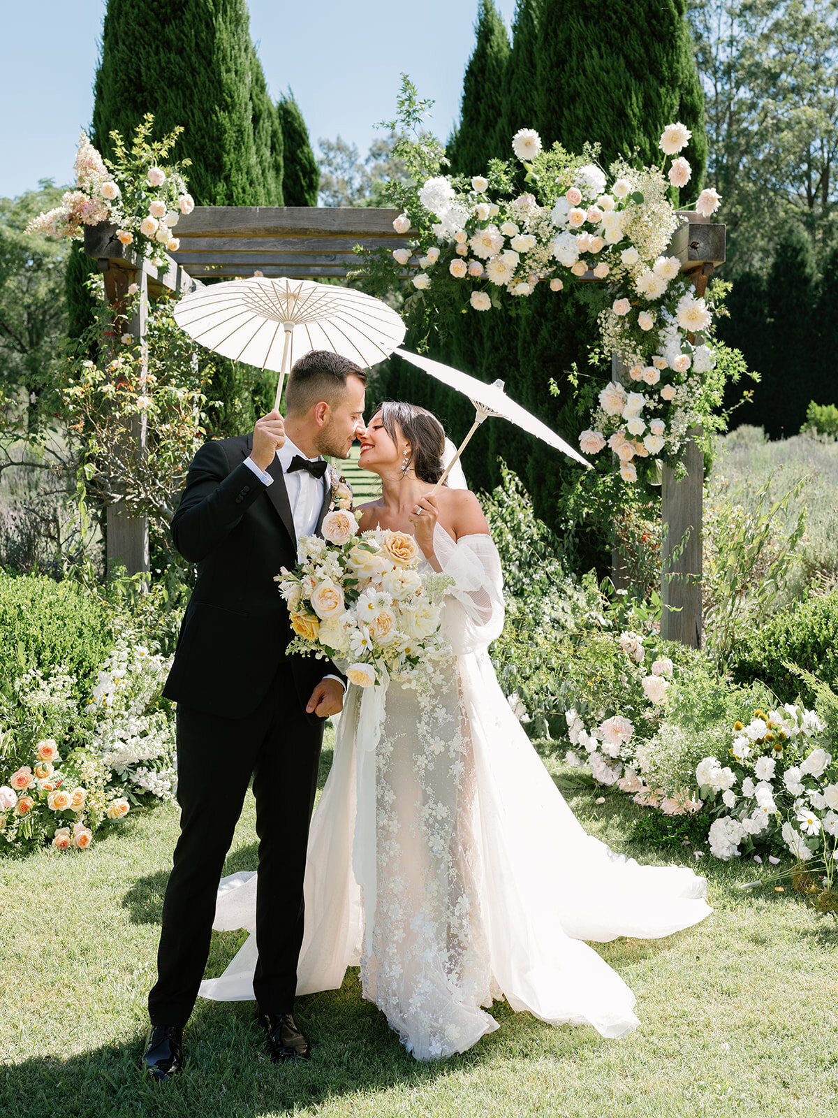 A couple kissing under a white parasol beneath a floral arbour