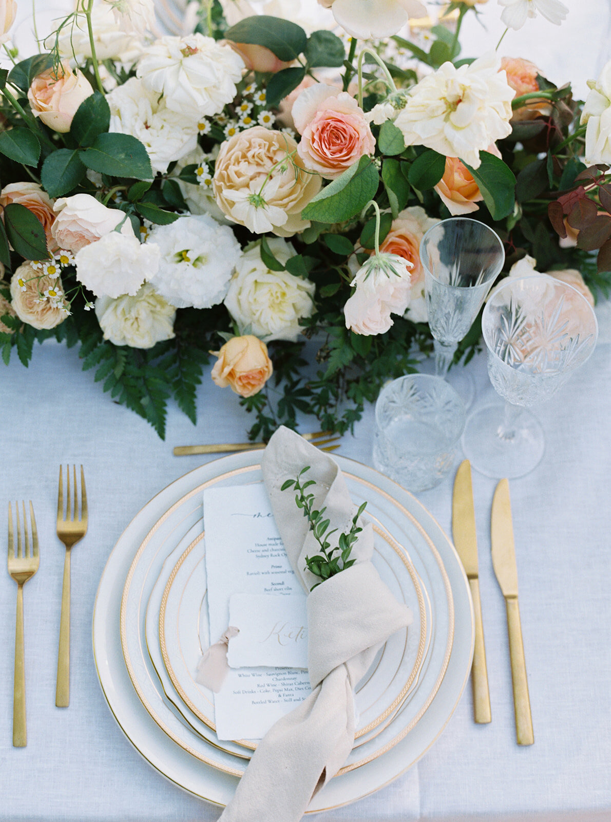 A place setting from above: gold cutlery, a linen napkin and a printed menu beside roses